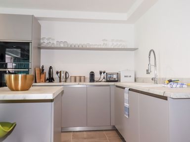 A kitchen with grey cabinets a marble countertop a metal bowl a sink toaster kettle and shelf with glasses at 30 Cliff Edge in Newquay
