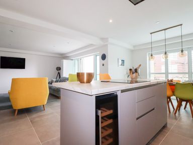 A modern open kitchen and living area with a kitchen island a wine fridge yellow and green chairs and a dining table at 30 Cliff Edge in Newquay