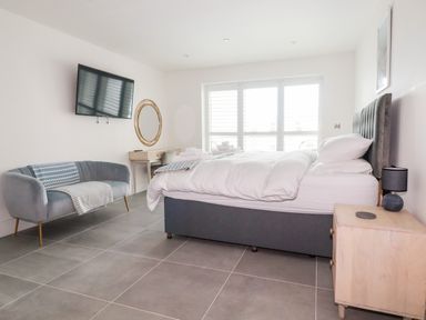 A bedroom with a bed a side table a sofa a wall mounted tv and a window at 30 Cliff Edge in Newquay