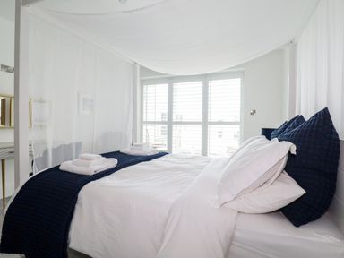 A bedroom with a four-poster bed with white linens and navy blankets near windows with white shutters at 30 Cliff Edge in Newquay