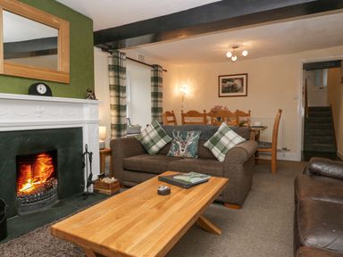 A living room with a fireplace two sofas a wooden coffee table and a dining table in the background at Nook Cottage in Rosthwaite near Keswick