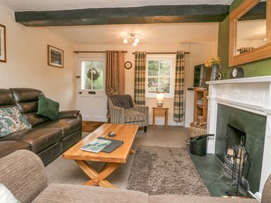 A living room with a leather sofa a wooden coffee table an armchair a fireplace and a window with curtains at Nook Cottage in Rosthwaite near Keswick