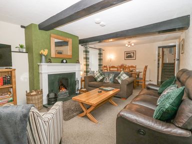 A living room with a fireplace a wooden coffee table sofas and a dining table at Nook Cottage in Rosthwaite near Keswick