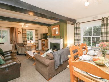 A living room with sofas a fireplace a TV and a dining table set with plates and fruit at Nook Cottage in Rosthwaite near Keswick