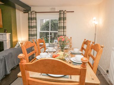 A dining table set with plates bowls glasses and a fruit bowl in a room with plaid curtains and a floor lamp at Nook Cottage in Rosthwaite near Keswick