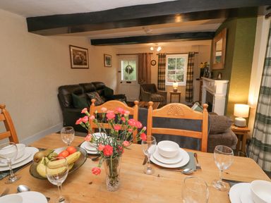 A dining table set with plates glasses and a vase of flowers in a living room with sofas and a fireplace at Nook Cottage Rosthwaite near Keswick