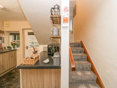 A kitchen with countertop appliances and shelves next to a carpeted staircase with wooden handrail at Nook Cottage in Rosthwaite near Keswick