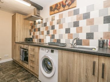 A kitchen with wooden cabinets a washing machine a sink an oven stovetop and tiled backsplash at Nook Cottage in Rosthwaite near Keswick