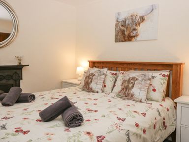 A bedroom with a wooden bed frame floral bedding pillows with animal prints bedside tables and a lamp at Nook Cottage Rosthwaite near Keswick