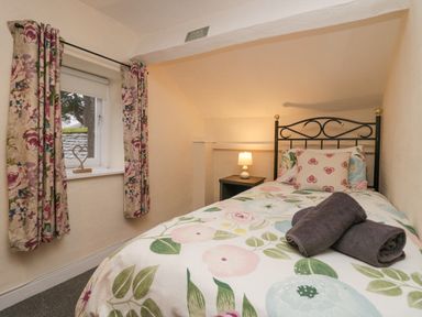 A small bedroom with a single bed floral curtains and a nightstand with a lamp at Nook Cottage Rosthwaite near Keswick