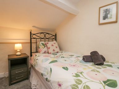 A small bedroom with a single bed floral bedding bedside table with lamp and framed picture on the wall at Nook Cottage in Rosthwaite near Keswick