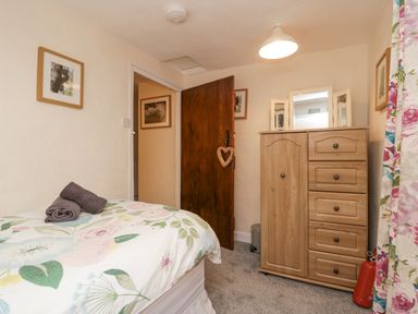 A bedroom with a bed with floral bedding a wooden chest of drawers a wooden door with a heart decoration and framed pictures on the walls at Nook Cottage Rosthwaite near Keswick
