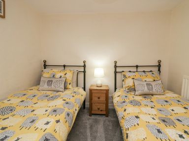 A bedroom with two single beds with yellow sheep patterned bedding and a wooden nightstand with a lamp between them at Nook Cottage in Rosthwaite near Keswick