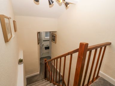 A staircase with wooden banister leading to a hallway with framed pictures on the walls at Nook Cottage in Rosthwaite near Keswick