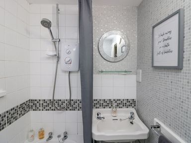 A bathroom with a shower, white tiled walls, a sink, a round mirror, and a framed quote at Nook Cottage in Rosthwaite near Keswick