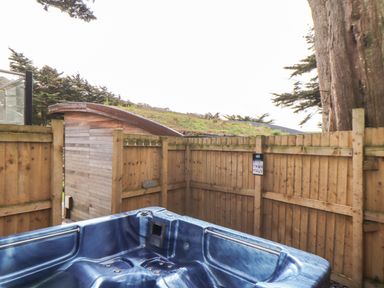 An outdoor blue hot tub next to a wooden fence with trees and a small wooden shed visible at 11 Towan Valley in Porthtowan