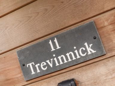 A house nameplate showing number 11 and the name Trevinnick attached to a wooden wall at 11 Towan Valley in Porthtowan