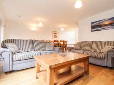 A living room with two striped sofas a wooden coffee table and a dining table with chairs at 11 Towan Valley in Porthtowan
