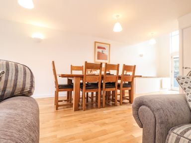 A dining area with a wooden table and six chairs in a room with light walls and wooden floor at 11 Towan Valley in Porthtowan
