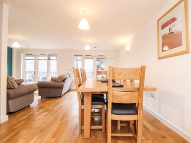 A dining area with wooden table and chairs adjacent to a living room with sofas and a coffee table at 11 Towan Valley in Porthtowan