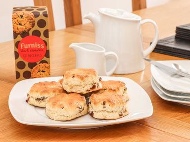 A plate of scones with a white teapot and milk jug on a wooden table at 11 Towan Valley in Porthtowan