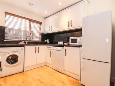 A kitchen with white cabinets a washing machine a dishwasher a microwave a kettle and a refrigerator at 11 Towan Valley in Porthtowan
