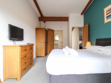 A bedroom with a bed towels on it a wooden dresser a wall-mounted television wooden wardrobe and an open door showing a bathroom at 11 Towan Valley in Porthtowan