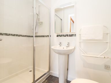 A bathroom with a shower enclosure a pedestal sink a wall-mounted mirror and a towel rack with a towel at 11 Towan Valley in Porthtowan