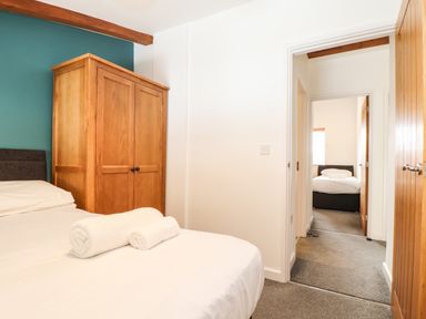 A bedroom with a bed and wooden wardrobe and an open door showing another bedroom at 11 Towan Valley in Porthtowan