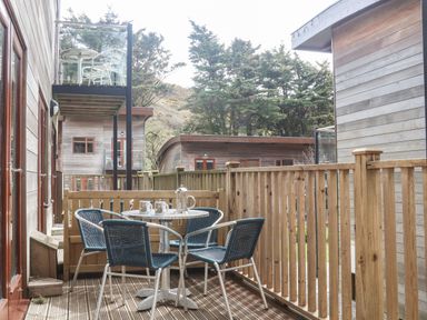 An outdoor wooden deck with a round table and four chairs surrounded by wooden railings at 11 Towan Valley in Porthtowan