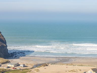 A beach with waves crashing on the shore near rocky cliffs and small buildings at 11 Towan Valley in Porthtowan