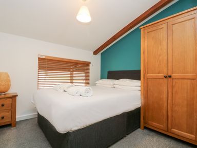 A bedroom with a bed white linens rolled towels wooden wardrobe bedside table and lamp at 11 Towan Valley in Porthtowan
