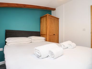 A bedroom with a bed with white linens and towels rolled on it a wooden wardrobe and teal accent wall at 11 Towan Valley in Porthtowan