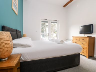 A bedroom with a bed with white sheets towels on top a wooden chest of drawers and a wall-mounted TV at 11 Towan Valley in Porthtowan