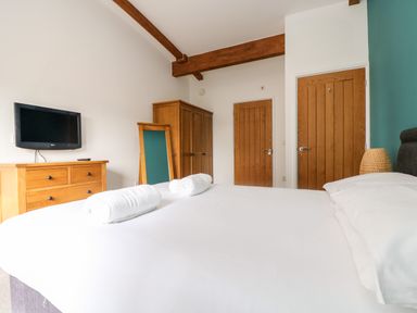 A bedroom with a bed towel rolls wooden dresser mirror wardrobe two doors and a wall-mounted TV at 11 Towan Valley in Porthtowan