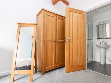 A bedroom corner with a wooden wardrobe, a full-length mirror, and an open door leading to a bathroom with a sink and shower at 11 Towan Valley in Porthtowan