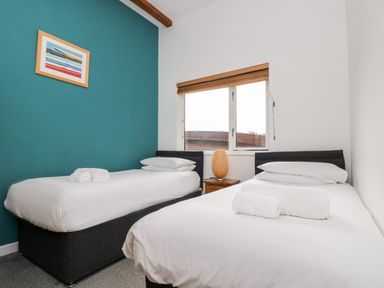 A bedroom with two single beds a window and a bedside table with a lamp at 11 Towan Valley in Porthtowan