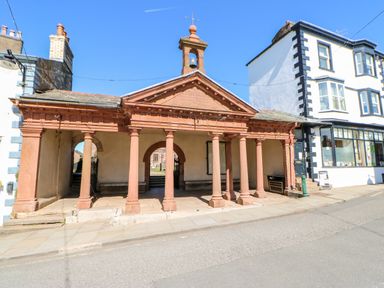A stone market hall with columns and a bell tower next to white buildings on a street at Summerseat in Kirkby Stephen