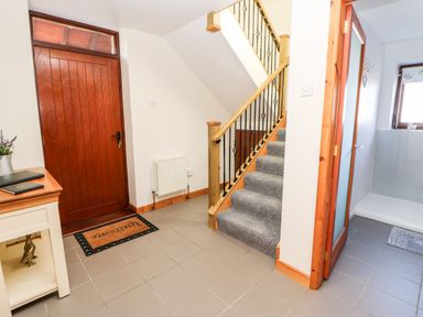 An entrance area with a wooden front door a staircase with carpeted steps a small table with books and a vase next to a tiled floor and a shower room at Summerseat in Kirkby Stephen