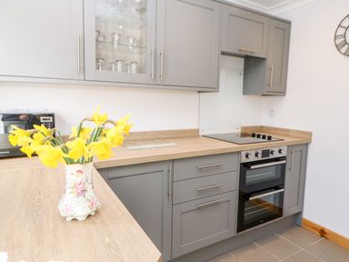 A kitchen with grey cabinets a wooden countertop a stove and a vase with yellow flowers at Summerseat in Kirkby Stephen