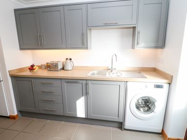 A kitchen with gray cabinets a double sink a washing machine and a countertop with a toaster fruit bowl and kettle at Summerseat in Kirkby Stephen