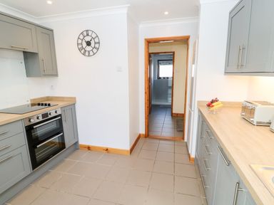 A kitchen with grey cabinets a built-in oven stove a wall clock and a doorway leading to another room at Summerseat in Kirkby Stephen