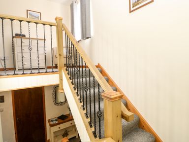 A staircase with a wooden handrail and black balusters next to a beige wall with framed pictures at Summerseat in Kirkby Stephen
