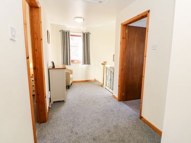 A carpeted hallway with wooden door frames a white cabinet and a window with curtains at Summerseat in Kirkby Stephen