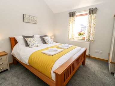 A bedroom with a wooden bed with yellow and white bedding and patterned curtains at Summerseat in Kirkby Stephen