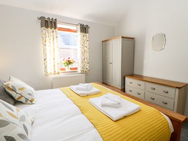 A bedroom with a bed covered with yellow bedding and white towels beside a dresser and wardrobe at Summerseat in Kirkby Stephen