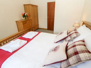 A bedroom with a wooden bed with pillows and folded towels a wooden dresser and wardrobe with flowers on top at Summerseat in Kirkby Stephen