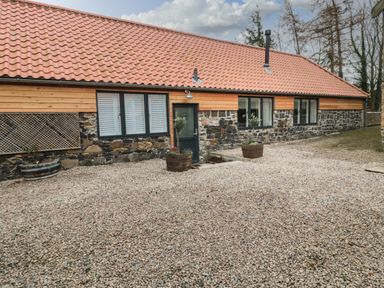 A single story building with a tiled roof stone and wood walls and gravel in front at The Bakery in Middleton near Belford