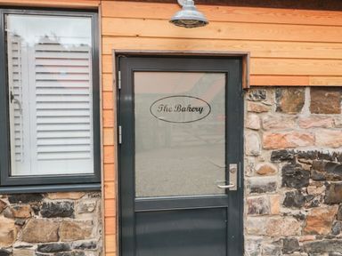A black door with frosted glass and the words The Bakery on it next to a window with white shutters on a stone and wood exterior at The Bakery in Middleton near Belford