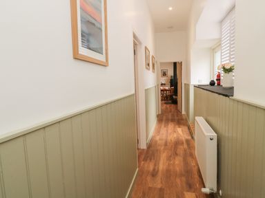 A hallway with wooden flooring and framed pictures on walls with green paneling at The Bakery in Middleton near Belford